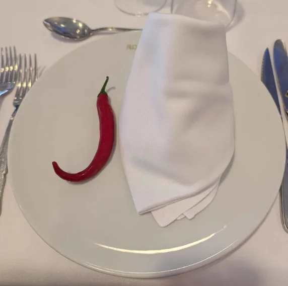 Un pimiento rojo sobre un plato blanco, junto a una servilleta, en la mesa de la comida.